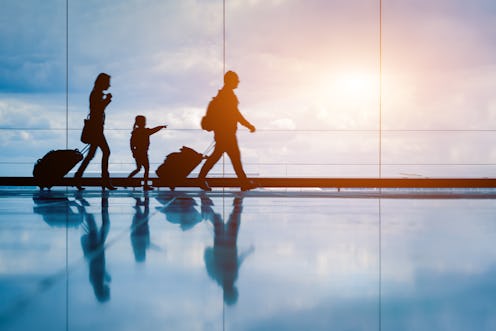 Family at airport travelling with young child and luggage walking to departure gate, girl pointing a...