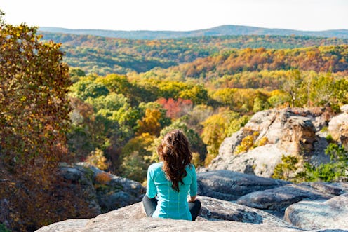 Woman meditating on cliff overlooking fall forest