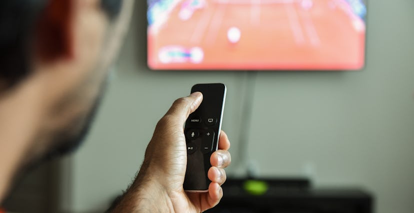 Man using remote control to switch channels. Close up hand holding apple tv remote