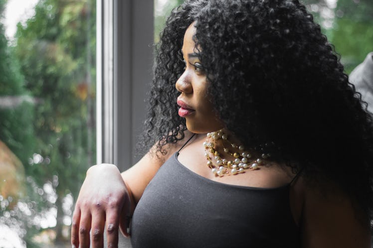 A young and stylish dark-skinned girl with curly hair sitting in a cafe near window