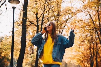 Autumn walk. Technologies. Happy girl in jean jacket and sunglasses is talking on the mobile phone a...