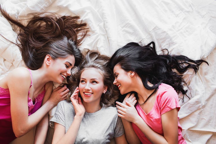 Top view of three best friends tell secrets in bed . Group of pretty young women in pajamas lie...
