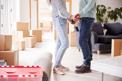 Close Up Of Loving Couple Holding Hands Surrounded By Boxes In New Home On Moving Day