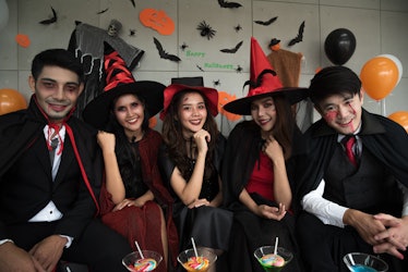 Group of young people in spooky Halloween costume with sweet candy and nectar on the table, October ...