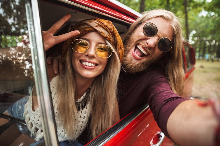 Photo of european hippie couple smiling and showing peace sign while driving retro minivan in forest