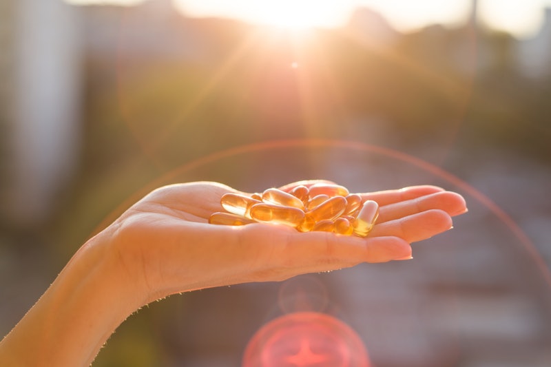 Hand of a woman holding fish oil Omega-3 capsules, urban sunset background. Healthy eating, medicine...