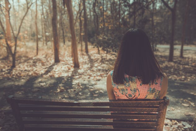 Sad woman sitting on the bench from back angle in the park vintage style,She passed the story lot wo...