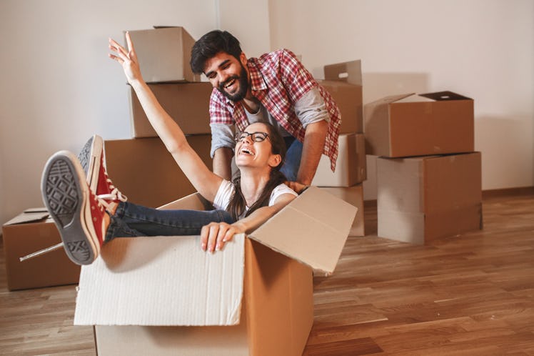 Young couple moving into a new home.Woman sitting in cardboard box while man pushes her all over the...