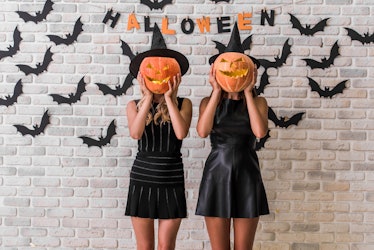 Beautiful girls in black dresses and witch hats are holding scary pumpkins, on background decorated ...