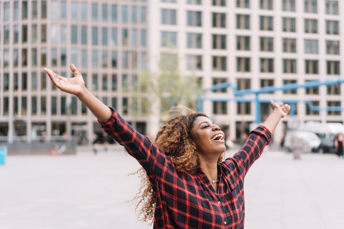 Joyful young African woman laughing and celebrating with open arms in an urban street with copy spac...