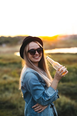 A blonde girl with sunglasses drinking beer at sunset and is very happy!