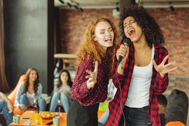 A group of friends sing karaoke into a microphone in their living room. 