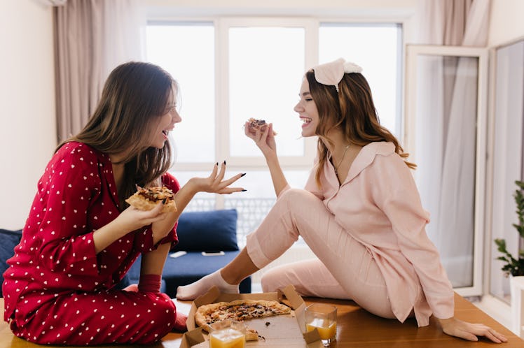 Inetersted girls talking around and eating cheese pizza. Indoor photo of lovable dark-haired ladies ...