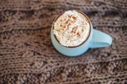 Mug of coffee, cocoa or hot chocolate with whipped cream and cinnamon on scarf. Pumpkin latte - cozy...