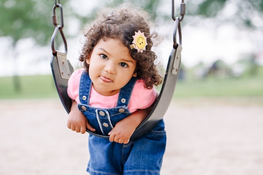 Portrait of happy smiling little latin hispanic toddler girl swinging on swings at playground outsid...