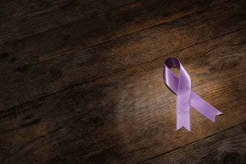 Purple ribbon on brown wooden background, space for text. Domestic violence awareness