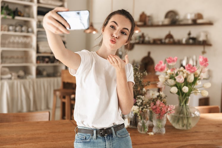 Image of attractive smiling woman wearing casual clothes taking selfie photo on cellphone and blowin...