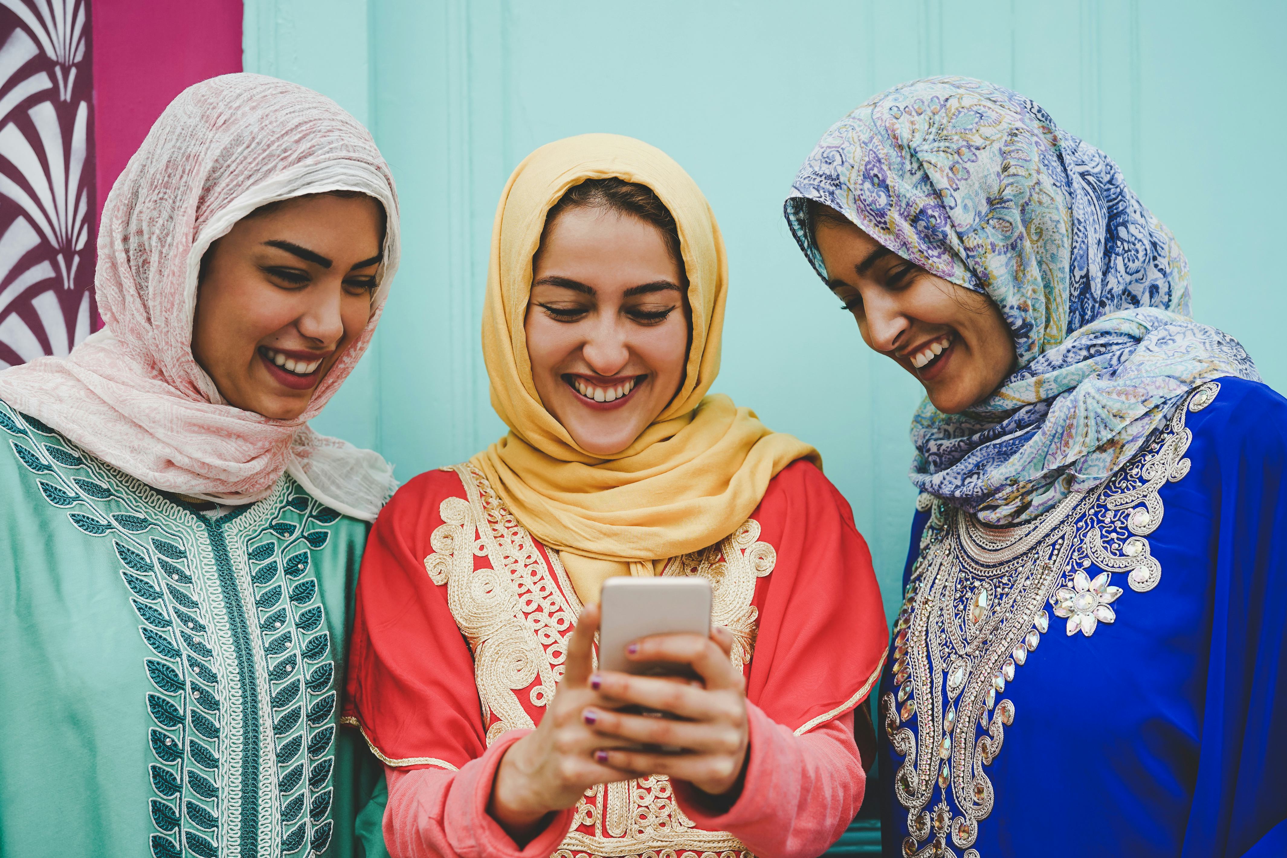 Happy Muslim women watching on mobile smart phone in the college - Arabian young girls having fun wi...