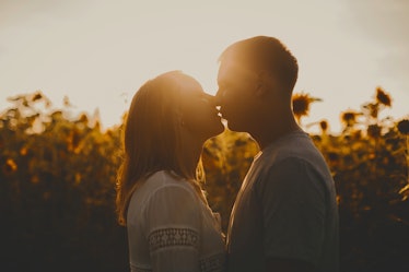 Beautiful couple in love is kissing at the sunset over a field of sunflowers. Summer vacation concep...