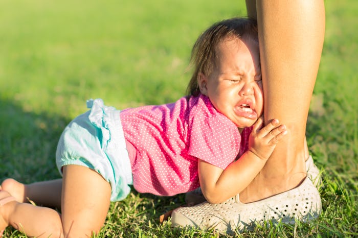 A baby crying holding on to her moms legs.
