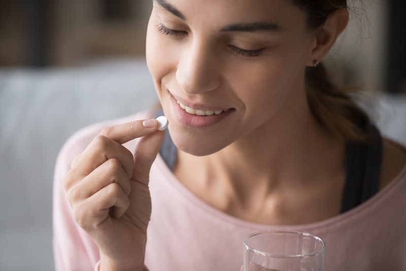 Close up face of healthy attractive woman holding pill and glass of water everyday taking omega 3, p...