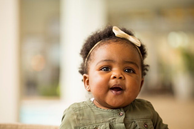 Baby girl in green smiling to camera in a story about Capricorn names.