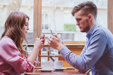 phubbing, always connected, internet addiction, young couple in cafe looking at their smartphones, s...