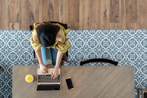 Top view of young asian woman sitting, using laptop in modern workplace, café coffee shop. Urban fem...