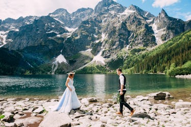 bride with the beautiful blue dress and groom with views of the beautiful green mountains and lake w...