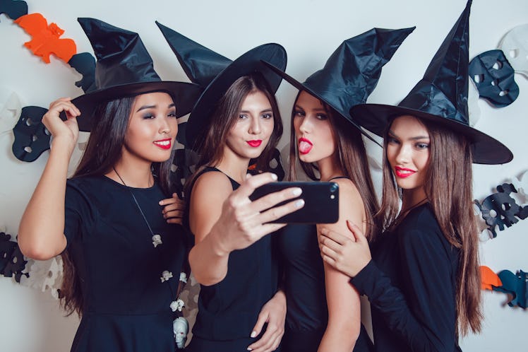 Women in witch halloween costumes standing and make selfie on white background.