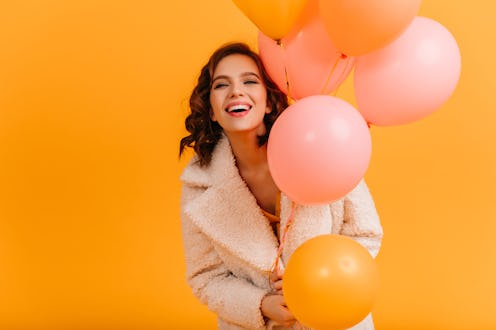 Attractive young woman holding pink balloons and smiling. Studio shot of blissful birthday girl isol...