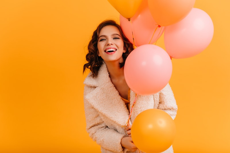 Attractive young woman holding pink balloons and smiling. Studio shot of blissful birthday girl isol...
