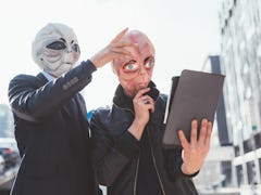 Two man wearing alien masks using tablet hand hold outdoor in city back light - strange, technology,...