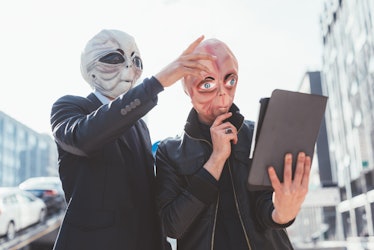 Two man wearing alien masks using tablet hand hold outdoor in city back light - strange, technology,...