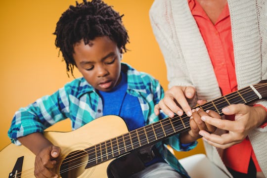 Boy learning how to play the guitar with the help of a teacher