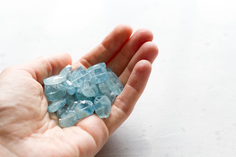 Aquamarine stone lies in the hand. Natural stone Aquamarine on a white background. Female hand. Copy...