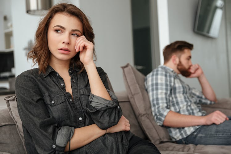 Photo of young sad quarrel loving couple sitting on sofa indoors. Looking aside.