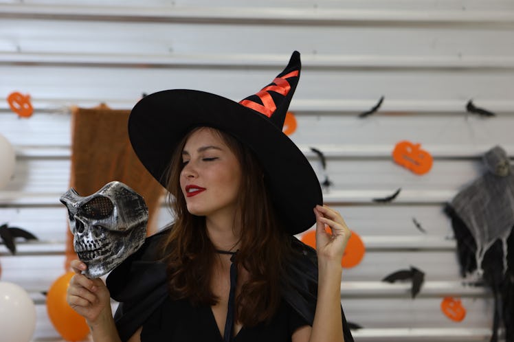 Halloween Witch with a  mask. Beautiful young surprised woman in witches hat and  holding mask. 
