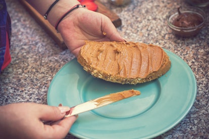 Young women spreading peanut butter on bread while preparing healthy sweet toasts for the breakfast