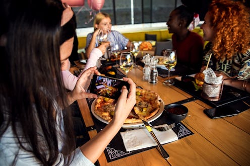 Group of young friends having fun in restaurant, talking and laughing while dining at table. Girl ta...