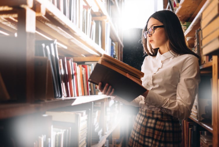 people, knowledge, education and school concept - happy student girl or young woman with book in lib...