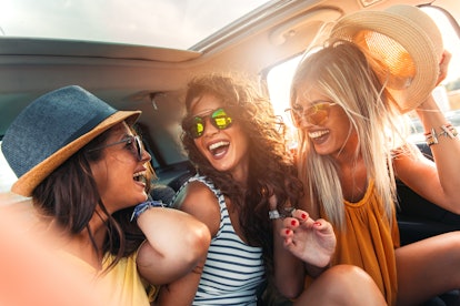Three female friends enjoying traveling in the car. Sitting in rear seat and having fun on a road tr...
