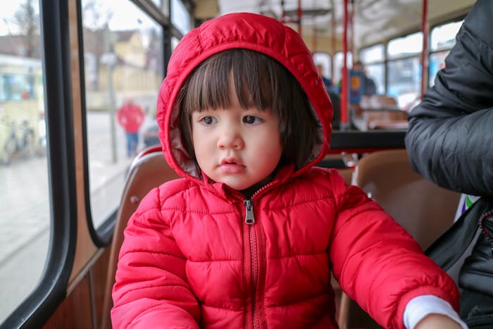 Little cute boy sitting on the bus looking out the window. he wearing red jacket with hooded