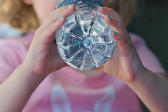 Close-up of a girl wearing a pink shirt drinking water out of a plastic bottle