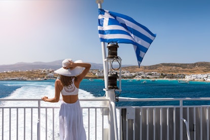 Woman in a white dress next to to a Greek flag on a ferry boat in the aegean sea, Greece