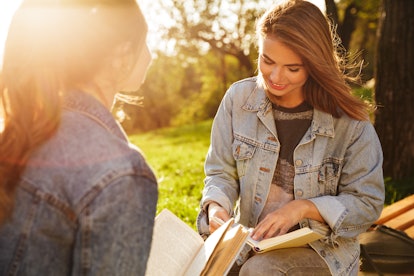 Close-up shot of two charming brunette female friends reading books in park at sunny day