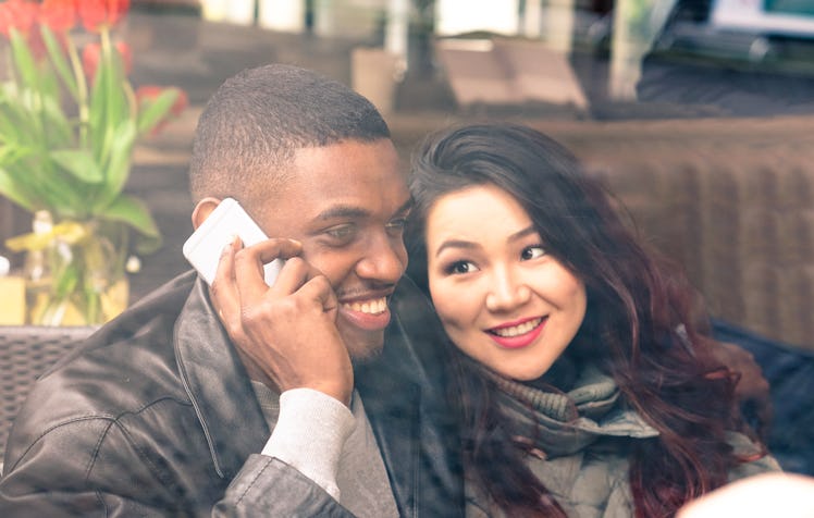 Interracial couple on date view through cafe window - Afro american man using phone and asian girlfr...