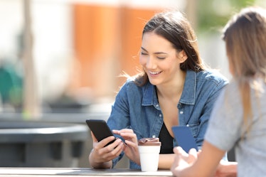 Happy woman checking smart phone online messages sitting in a park