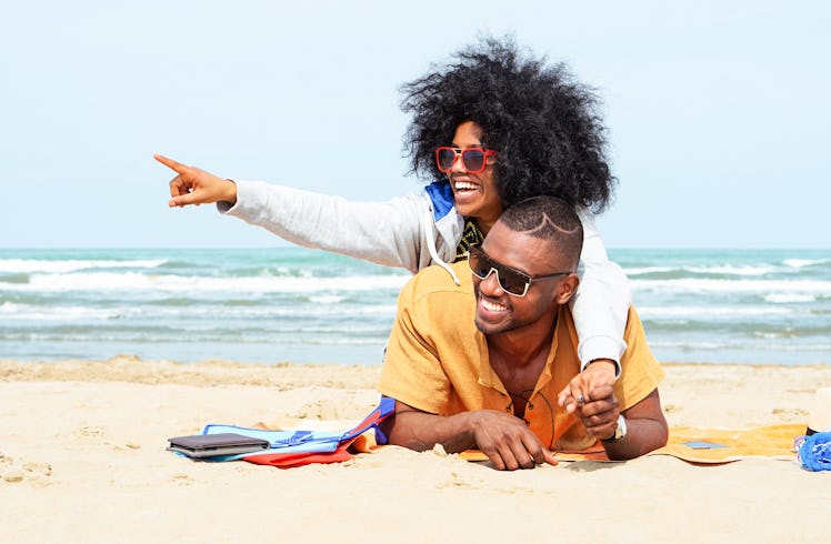 Young afro american couple  pointing finger relaxing on beach - Cheerful african friends having fun ...