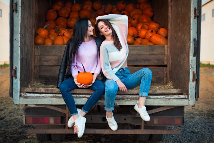 Fashionable beautiful young girlfriends together at the autumn pumpkin patch background. Having fun ...